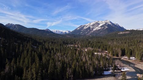 Majestic-scenic-shot-of-snow-capped-mountain-range,-river-and-evergreen-forest-in-Cle-Elum-on-a-blue-sky-day-in-Washington-State