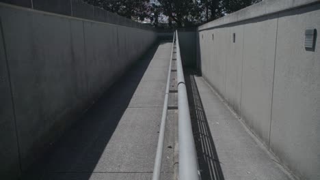 The-image-features-a-narrow,-concrete-pedestrian-ramp-flanked-by-high-walls,-converging-in-a-vanishing-point-perspective