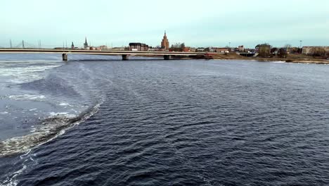 Aerial-of-bridge-pver-Daugava,-spans-a-river-with-a-Riga-city-in-the-background