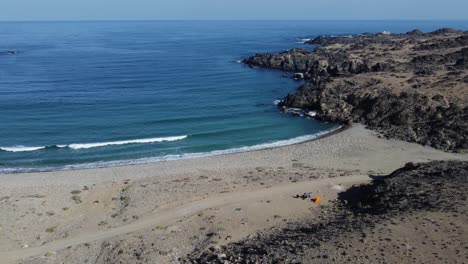 Motorradtourist-Mit-Orangefarbenem-Zelt-Ist-Allein-Am-Ruhigen,-Halbmondförmigen-Ozeanstrand