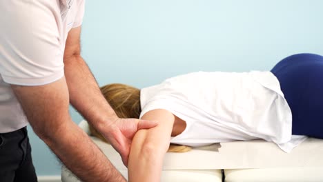 Physiotherapist-correcting-arm-of-woman-on-massage-table