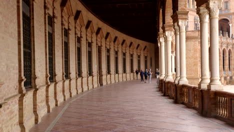Tourists-Strolling-Through-the-Interior-Corridor-of-Plaza-de-España,-Seville,-Spain---Static-Shot