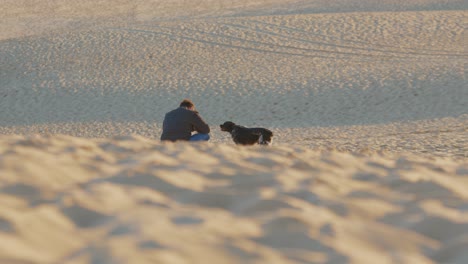 Man-Is-Sitting-On-The-Sand-Dune-With-His-Dog-In-Arcachon-Bay-During-Winter-In-France