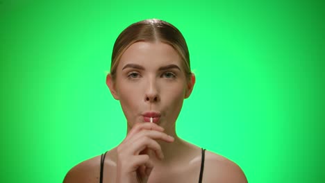 Woman-licks-lollipop,-looking-at-the-camera,-green-background,-slowmo