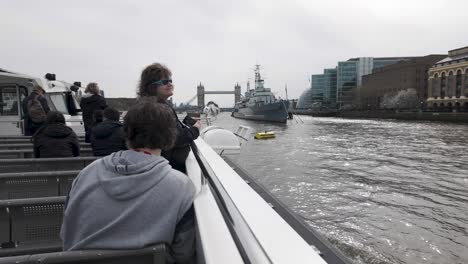 View-from-a-ferryboat-on-a-Thames-River-cruise-in-London,-nearing-HMS-Belfast-with-Tower-Bridge-in-the-backdrop,-embodying-the-spirit-of-travel-and-exploration