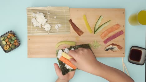 Top-shot-of-two-Hands-preparing-Sushi-on-blue-table