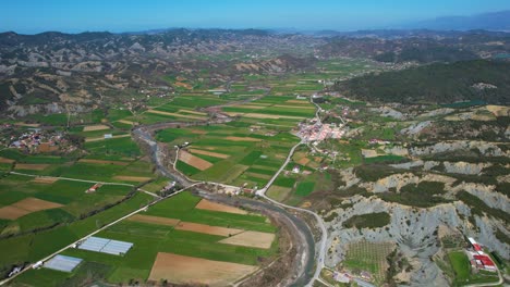 Tal-Inmitten-Sanfter-Hügel,-Die-Das-Dorf-Mit-Landwirtschaftlichen-Parzellen-An-Den-Ufern-Eines-Strömenden-Flusses-Im-Frühling-In-Albanien-Umgeben