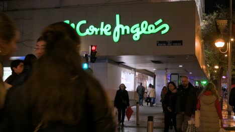 Pedestrians-cross-the-street-in-front-of-the-Spanish-biggest-department-store,-El-Corte-Ingles,-during-nighttime