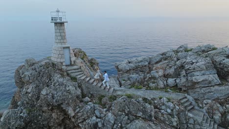 Kalamota-Island,-Adriatic-Sea,-Croatia---A-Couple-Making-Their-Way-to-the-Lighthouse-to-Admire-the-Sunset---Aerial-Pullback-Shot