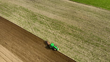 Green-Tractor-with-disk-plow,-plowing-countryside-field-during-sunlight-in-spring