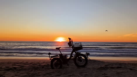 Silhouette-Eines-Elektrischen-Fahrrad-Dreirads-An-Einem-Strand-Bei-Sonnenuntergang