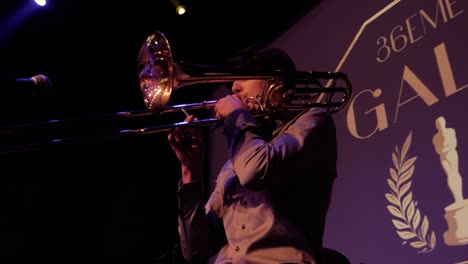 A-young-student-trumpet-player-plays-the-trumpet-on-stage,-he-has-a-microphone-in-front-of-him,-behind-him-the-gala-poster-of-his-student-promotion