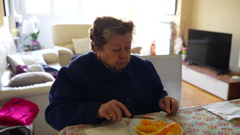 High-angle-wide-shot-of-old-woman-eating-orange-fruit-at-home,-living-room