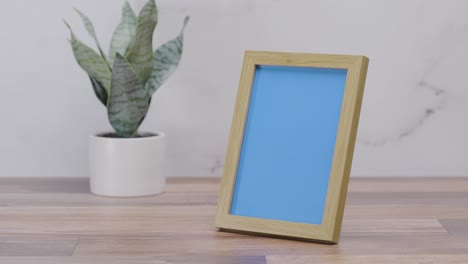Holzbilderrahmen-Auf-Der-Arbeitsplatte-Mit-Austauschbarem-Blauem-Bildschirm-Auf-Weißem-Hintergrund-|-4k