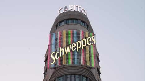 A-vibrant-Schweppes-neon-sign-adorns-the-Carrion-building,-known-as-the-Capitol,-on-Madrid's-Gran-Via,-a-bustling-hub-for-entertainment-and-retail