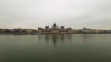 Day-to-night-time-lapse-of-Budapest-Parliament-under-a-hazy-sky,-showcasing-the-luminous-riverside-landmark