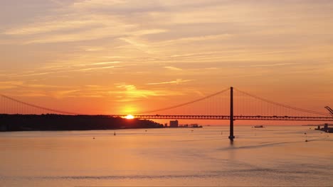 Panoramic-aerial-pan-as-sun-sets-below-hill-in-distance-of-Tagus-River-past-suspension-bridge-in-Lisbon-Portugal