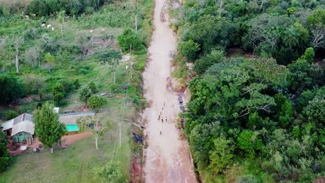 Luftaufnahme-Einer-Straße,-Die-Durch-Den-Paraguayischen-Wald-Führt,-Mit-Kindern,-Die-Bergauf-Zurück-Zu-Ihren-Häusern-Gehen
