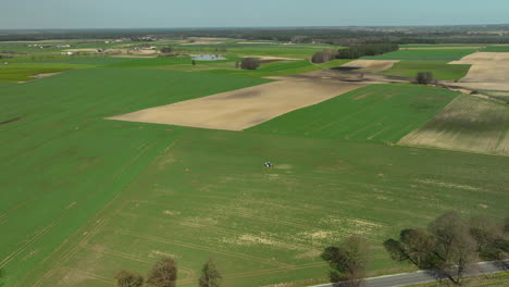 Luftaufnahmen-Zeigen-Ein-Flickwerk-Aus-Ackerland,-Auf-Dem-Ein-Einzelner-Traktor-Systematisch-Die-Pflanzen-Besprüht-Und-So-Zeichen-Des-Fortschritts-In-Die-Grüne-Landschaft-Zeichnet.