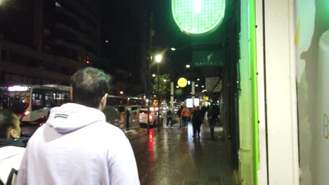 Rivadavia-Avenue,-Underground-line-A-of-Metro,-people-walk-at-night-Buenos-Aires-City,-metropolitan-area,-lighting-of-commercial-pharmacy-store,-buses-and-traffic