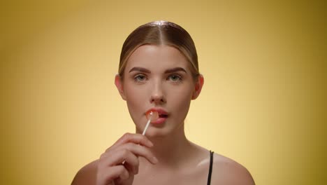 Portrait-beautiful-young-woman-licking-a-tasty-sweet-lollipop,-yellow-background