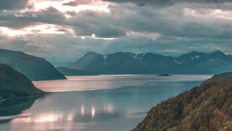 Rays-of-the-setting-sun-shine-through-the-storm-clouds-above-the-serene-fjord-in-a-timelapse-video