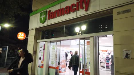 Farmacity-pharmacy-entrance-at-buenos-aires-argentina-medical-shop-at-night-town-landmark-for-goods-in-capital-city-of-argentina,-people-buyers-and-pedestrians-walking-by