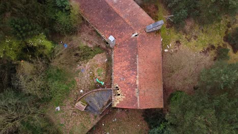 Top-down-aerial,-broken-roof-of-abandoned-house-in-the-belgian-pine-forest