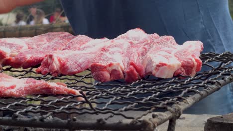 Close-up-view-placing-pieces-of-raw-meat-on-the-grill-for-a-barbecue-with-family-and-friends