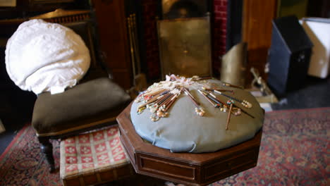 Victorian-pin-cushion-on-a-wooden-sewing-table,-with-lace-and-bobbins,-in-a-historical-home-setting