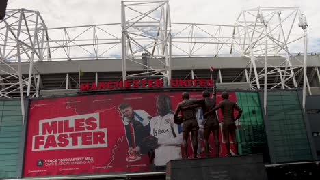 Statue-of-football-players-in-front-of-Old-Trafford-in-Manchester-under-cloudy-sky,-timelapse