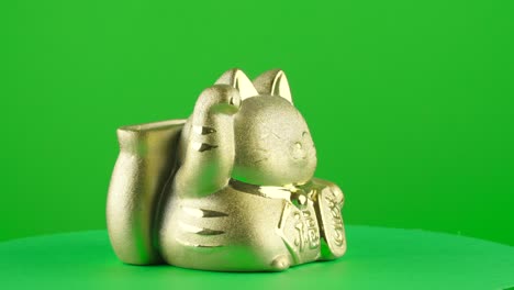 Goldene-Maneki-Neko-Spardose,-Sparschwein,-Glückliche-Japanische-Katze-Auf-Grünem-Hintergrund,-Chroma-Key-Hintergrund-Ersatz-Hintergrundobjekt-In-Einer-Drehscheibe,-3D-Drehschleife