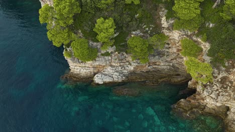 Isla-Kalamota,-Mar-Adriático,-Croacia---Aguas-Cristalinas-Contrastan-Con-La-Escarpada-Costa-Debajo-De-Los-Acantilados-Rocosos-Con-Vegetación---Toma-Aérea-De-Drones