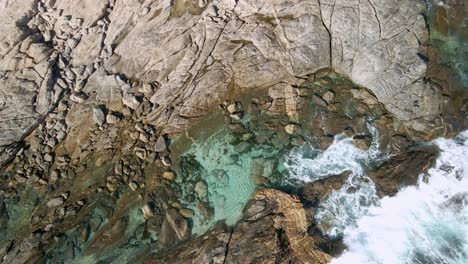 Tourist-swimming-in-beautiful-clear-rock-pool-alone-with-crashing-white-waves-drone-view,-Greenly-Beach,-Eyre-Peninsula,-South-Australia