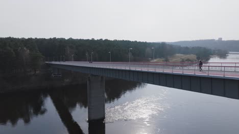 Die-Drohne-Gleitet-Seitwärts-Und-Erfasst-Eine-Von-Fußgängern-Belebte-Brücke,-Die-Die-Stadt-Mit-Dem-Wald-Verbindet