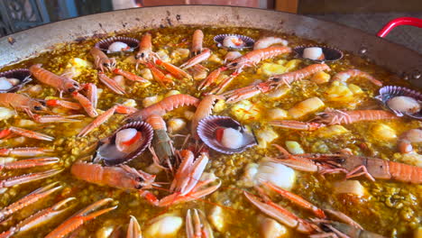 Kochen-Eines-Riesigen-Traditionellen-Spanischen-Paella-Gerichts-Mit-Meeresfrüchten,-Garnelen,-Jakobsmuscheln-Und-Kaisergranat-(Nephrops-Norvegicus),-Köstlich-Gekochter-Reis-Mit-Meeresfrüchten,-Marbella,-Spanien,-4K-Aufnahme