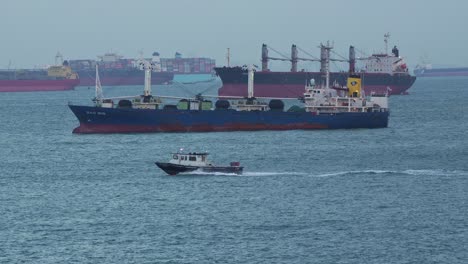 Barco-De-La-Autoridad-Gubernamental-Que-Navega-Alrededor-De-Los-Grandes-Buques-De-Carga-En-El-Estrecho-De-Singapur,-Inspeccionando-Las-Mercancías-Aduaneras-Y-Documentándolas-Antes-De-Que-Lleguen-Al-Interior.