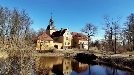 Lielstraupe-castle-on-a-sunny-spring-day,-approaching-aerial-view-above-the-pond