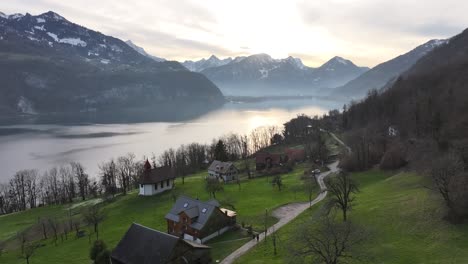 -The-beauty-of-Walensee-region-from-a-drone's-perspective,-capturing-the-serenity-of-lakeside-homes,-meandering-rivers,-and-majestic-snowy-peaks-under-the-glowing-sunrise