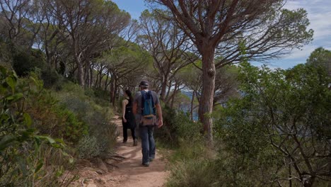 Tourists-walk-along-coastal-path-along-the-cliffs-mediterranean-sunny-landscape-green-environment-at-Sant-Feliu-de-Guixols,-skyline-background