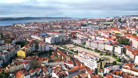 Volando-Hacia-Atrás-Sobre-La-Ciudad-De-Lisboa,-Con-Vistas-Desde-La-Plaza-Martim-Moniz,-Con-El-Paisaje-Urbano-De-Lisboa-Y-El-Río-Tajo-Al-Fondo,-Portugal