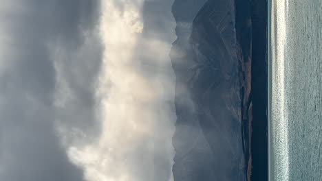 Sun-rays-shinning-through-the-clouds-over-Lake-Pukaki,-New-Zealand---vertical-time-lapse