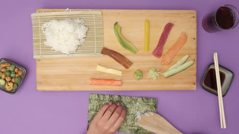 Draufsicht-Von-Zwei-Händen,-Die-Sushi-Auf-Einem-Violetten-Tisch-Zubereiten