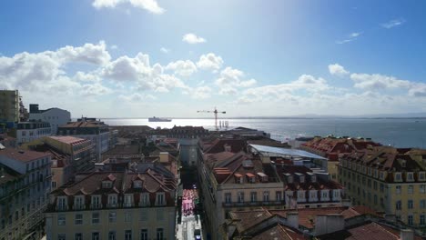 Rückwärts-Fliegen-über-Die-Rosa-Straße-In-Cais-Do-Sodre-In-Der-Stadt-Lissabon-Mit-Fliegenden-Möwen-Und-Dem-Fluss-Tejo-Als-Hintergrund-Und-Dem-Stadtbild-Von-Lissabon,-Portugal