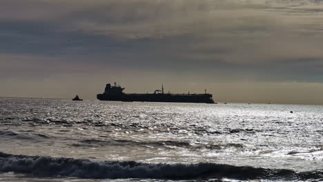 Silhouette-of-an-oil-tanker-far-in-the-sea-with-a-towing-boat