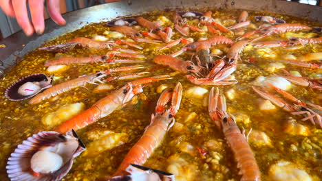 Cooking-a-big-traditional-Spanish-seafood-Paella-dish-with-shrimps,-St-Jacques-scallops-and-Cigala-Norway-lobsters-Nephrops-norvegicus,-cooked-rice-with-seafood,-Marbella-Spain,-4K-shot