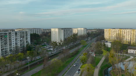 aerial-view-of-a-suburban-residential-area-in-Żabianka,-Gdańsk,-with-large-apartment-buildings-flanking-a-road-amidst-green-spaces-and-trees,-under-a-soft-evening-sky