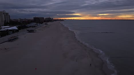 An-aerial-time-lapse-over-the-beach-at-Coney-Island,-NY-during-a-cloudy-and-colorful-sunrise