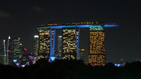 Singapore-city-skyline,-modern-architecture-of-Marina-bay-sands,-a-5-star-integrated-resort-hotel-with-vivid-lights-and-light-up-Supertree-grove-at-Gardens-by-the-bay-at-night