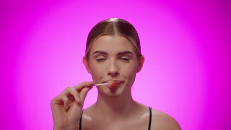 Portrait-woman-looking-at-camera-and-licking-confectionary-lollipop,-studio